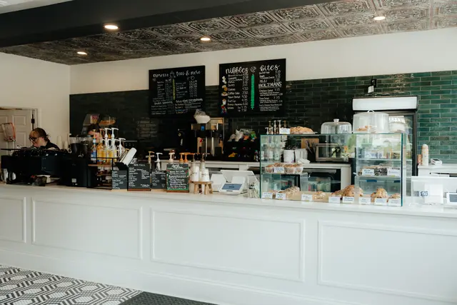 Birdie’s order counter with white paneled front, green subway tile wall, chalkboard drink and food menus, pastry case, and pressed-tin ceiling.