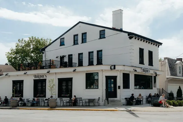 Birdie’s corner café on a sunny day—white brick, black trim, sidewalk seating with guests and planters.