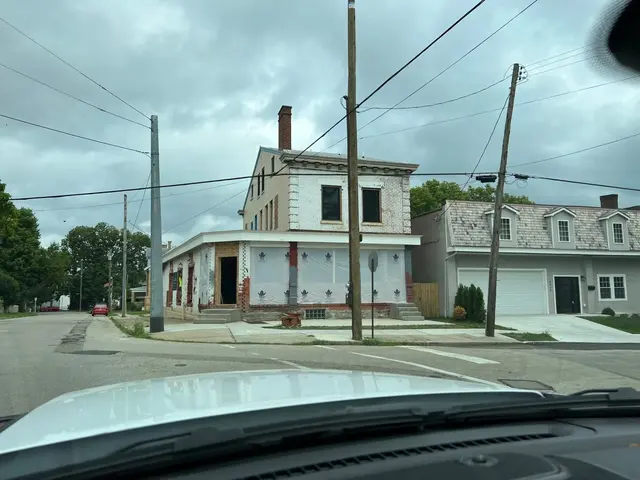 Wide view from a car of the corner building with ground floor wrapped in white protective sheet and new concrete steps.
