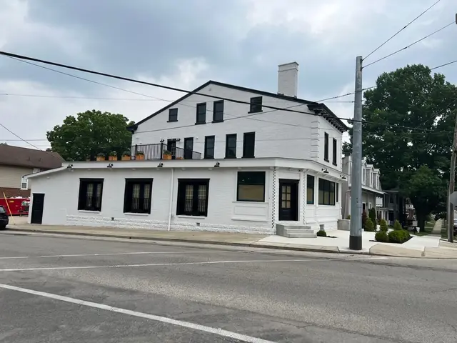 Elevated view of finished white brick corner building with black-trim windows, rooftop planters, and landscaped sidewalk.