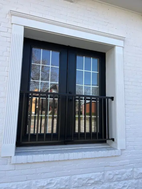 Ground-floor pair of black French doors with divided glass in a white brick opening; metal railing across the threshold.