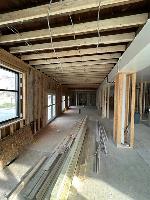 Long bay with new ceiling joists, stacked lumber on concrete floor, and French doors letting in daylight.