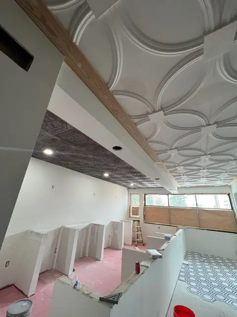 Interior under finish-out: circular embossed ceiling tile, dark tin soffit with recessed lights, hex tile floor partially exposed.