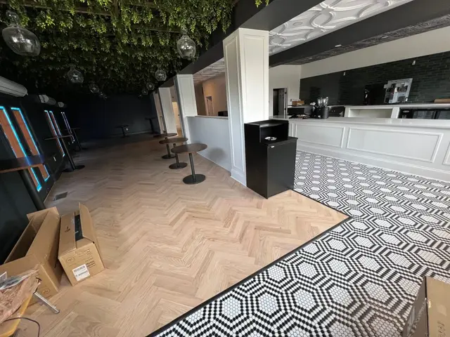 Nearly finished café with greenery draped ceiling, teardrop pendants, herringbone wood floor, and long white service counter.