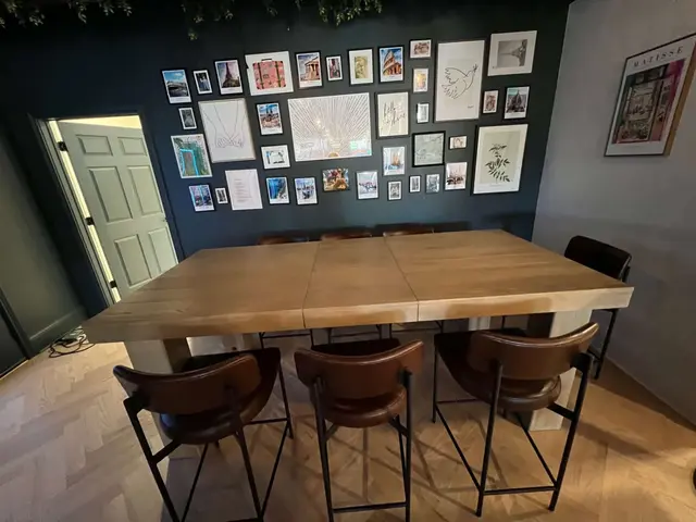Long communal wood table with leather chairs facing a dark gallery wall of framed travel photos and prints.